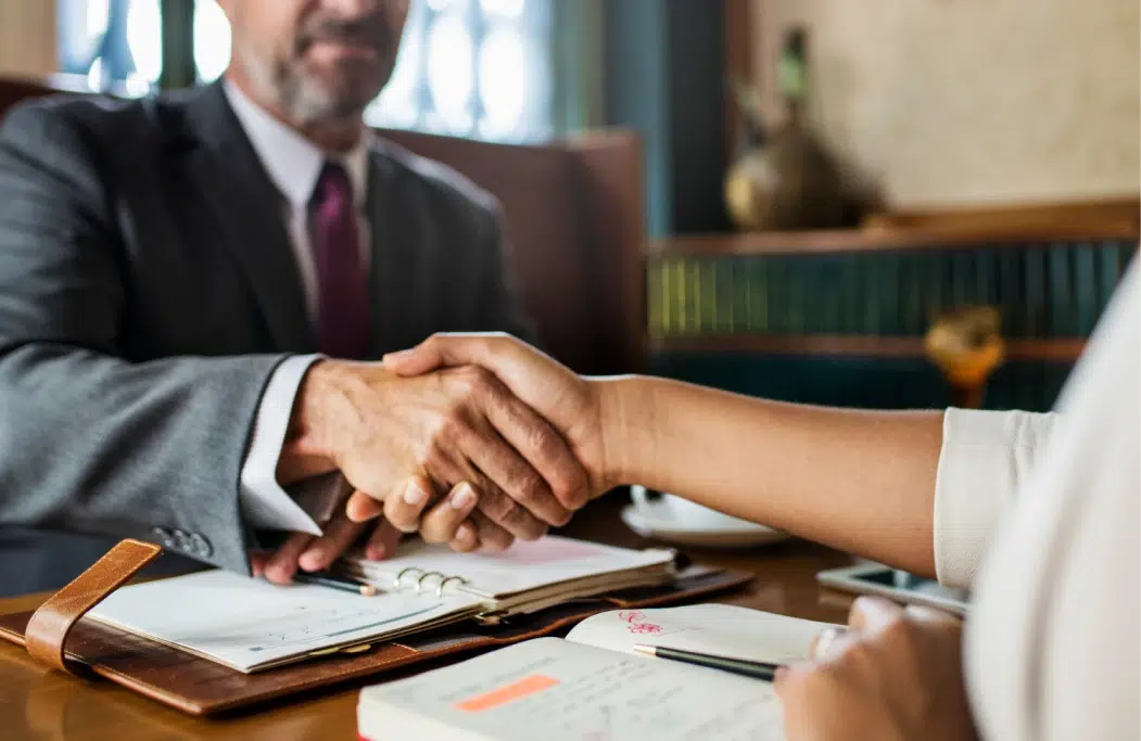 Two people shaking hands across a table.